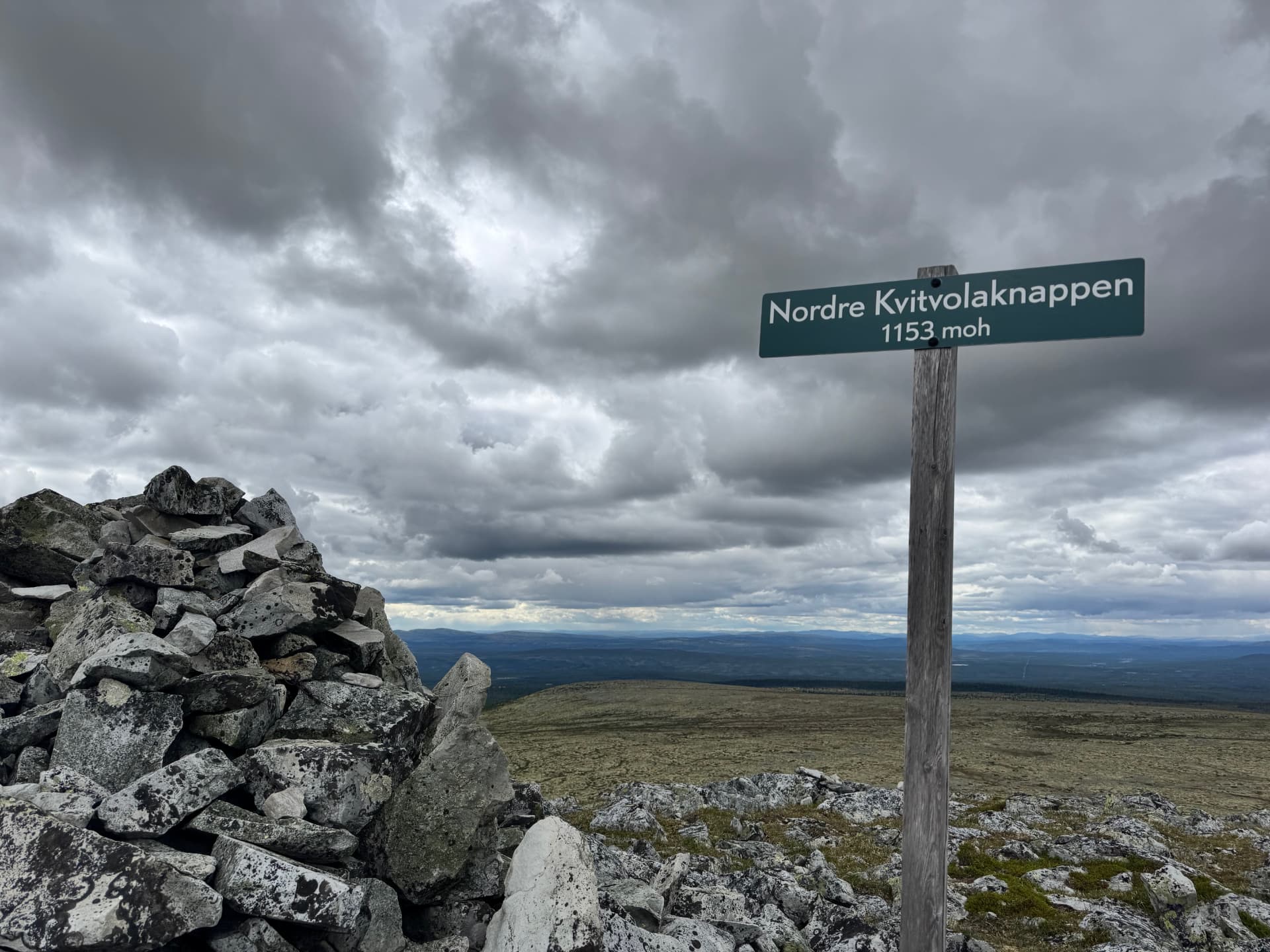 Summit sign reading Nordre Kvitvolaknappen 1153 moh next to a stone cairn