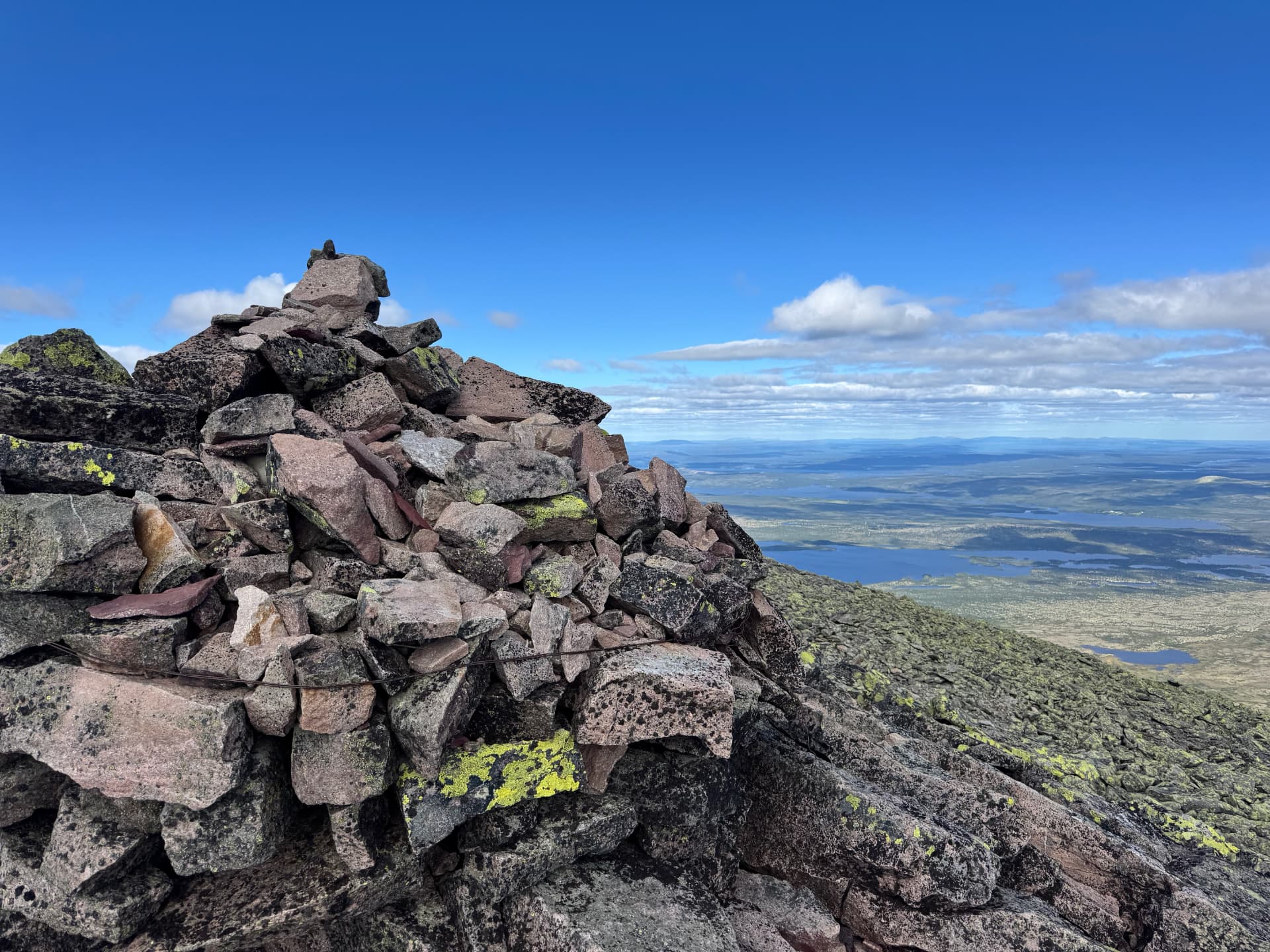 Summit cairn on Sølentoppen with a lake and low blue mountains visible in the distance under a clear sky