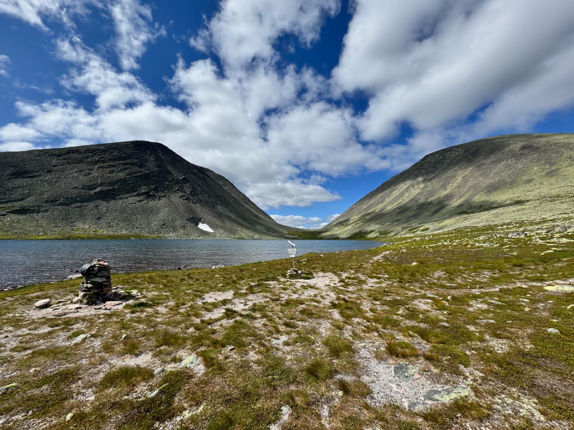 Skardstjønna mountain lake sitting between two dark rocky ridges with a small cairn and trail sign in the foreground