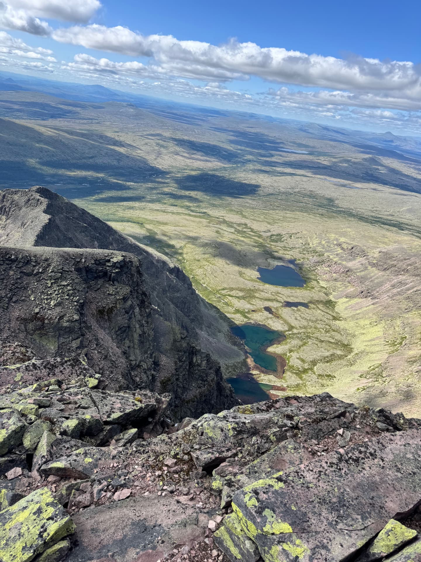 Aerial-like view from the summit ridge down into a deep cirque with turquoise and dark blue tarns far below