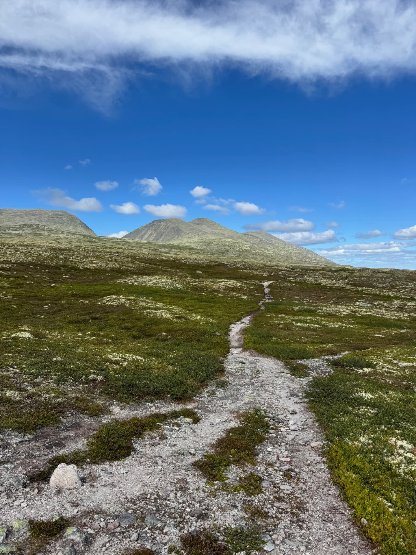 Rocky trail crossing open mountain plateau towards the V-shaped Sølenskardet notch between two summits