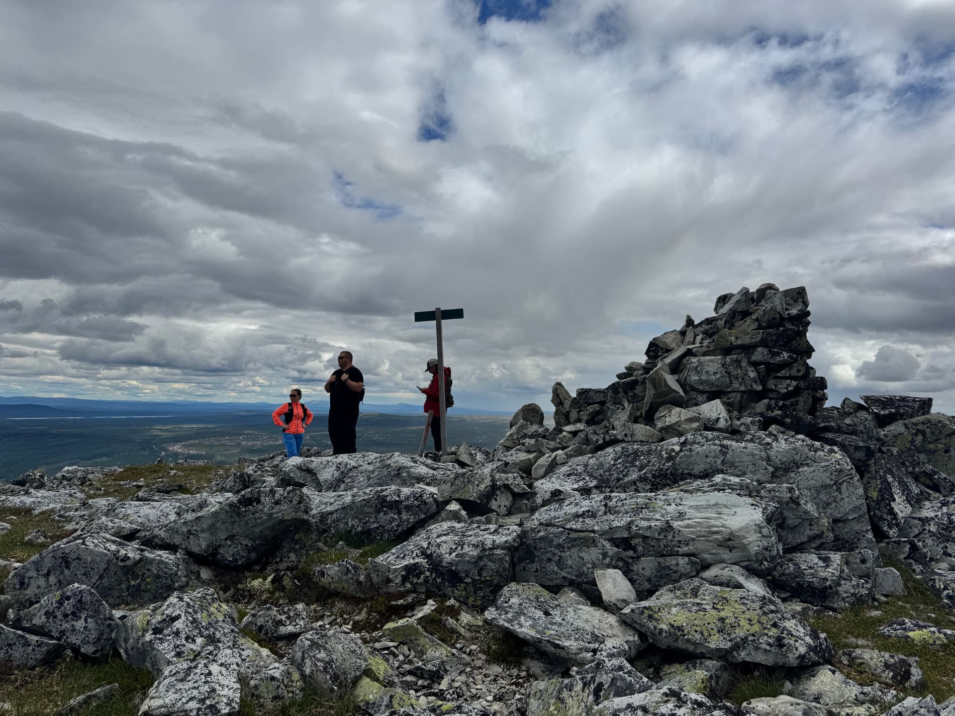 Three hikers standing beside the summit cairn and sign on Nordre Kvitvolaknappen