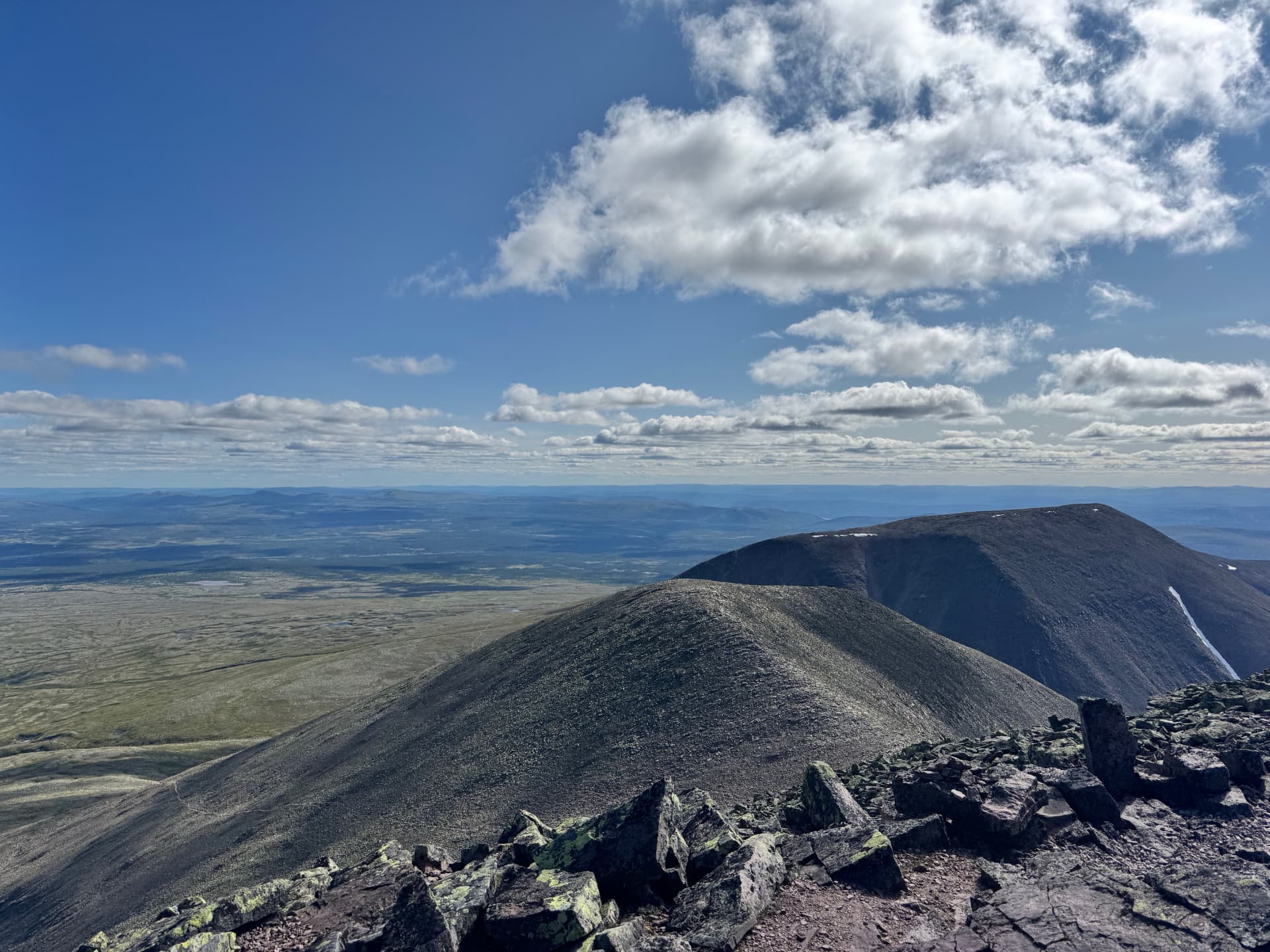 The rounded scree-covered ridge of Søre Sølen seen from Sølentoppen with plateau and distant blue hills beyond